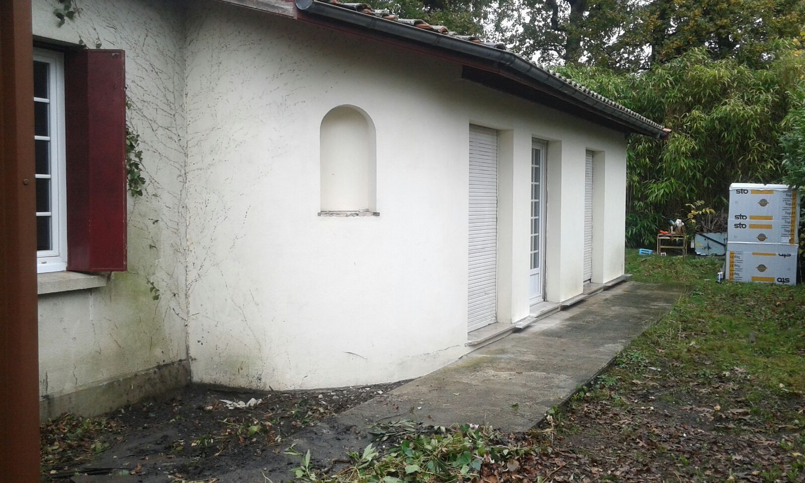L'extérieur d'une maison blanche de plain-pied, avec une partie de mur arrondie, avant ravalement.