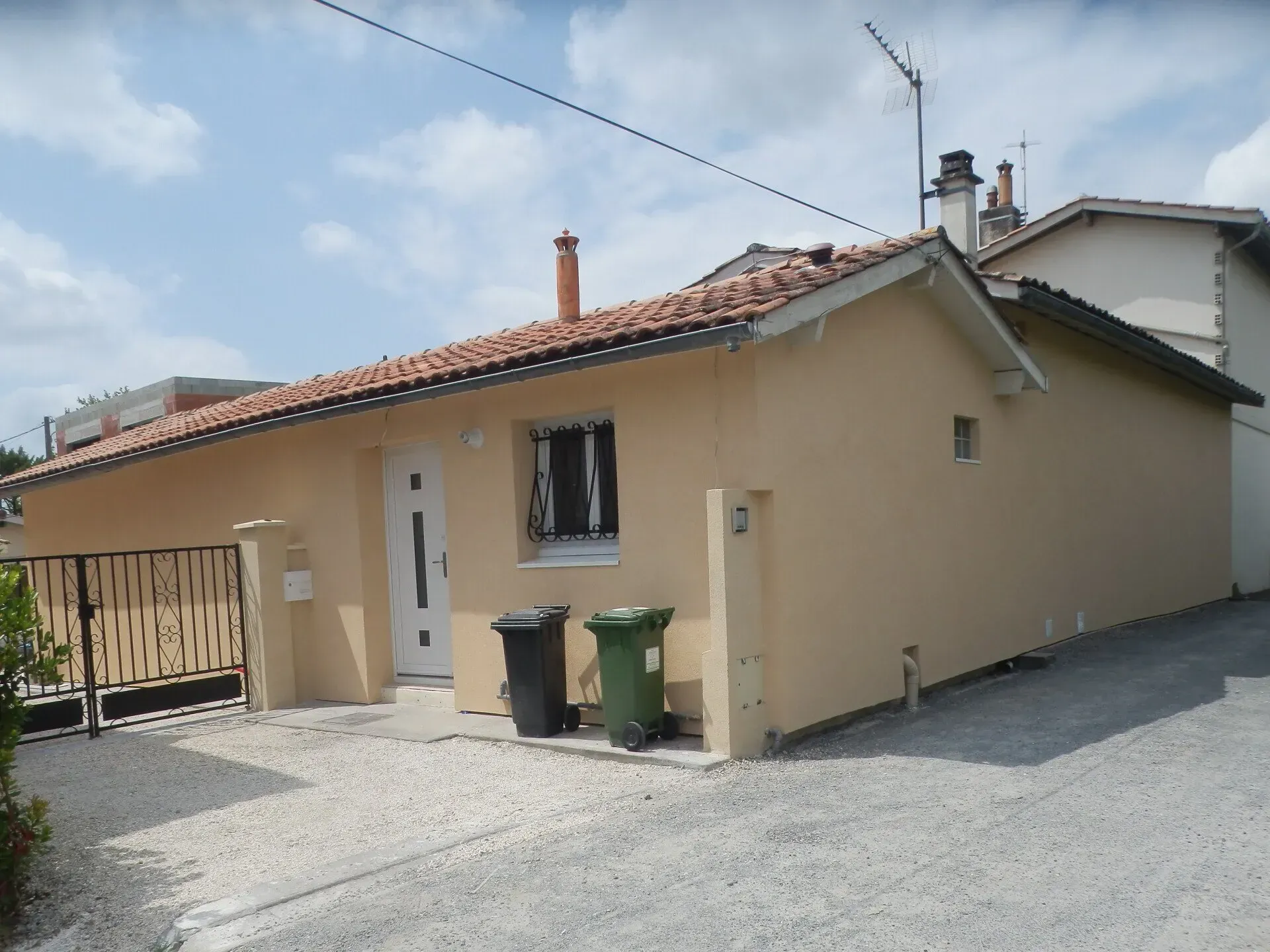 Une petite maison beige de plain-pied avec un toit de tuiles et une porte d'entrée blanche, après rénovation de façade.