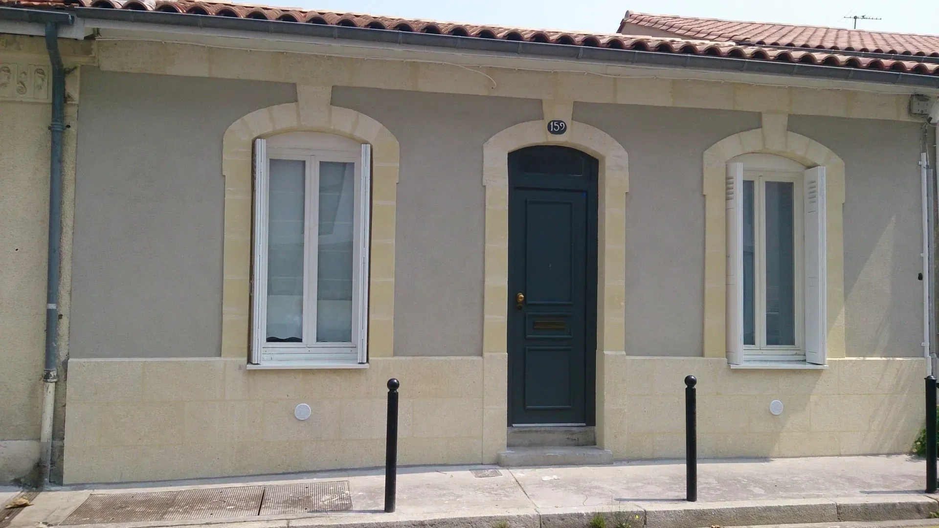 Une façade de maison avec une porte rouge flanquée de deux fenêtres, après ravalement.