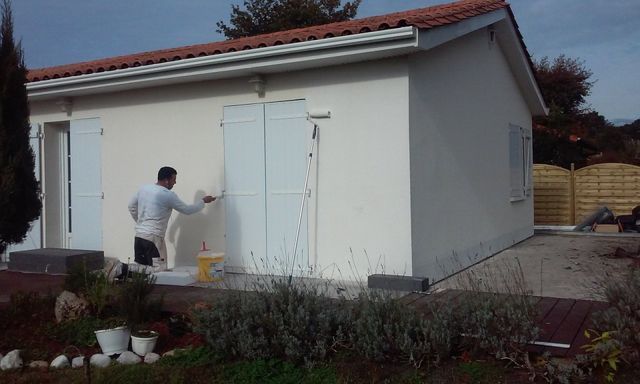 Une personne peint l'extérieur d'une maison blanche.