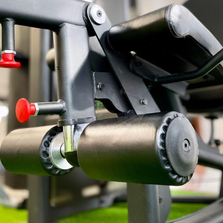 Primer plano de los rodillos acolchados y los brazos de palanca de una máquina de extensión de piernas en un gimnasio.