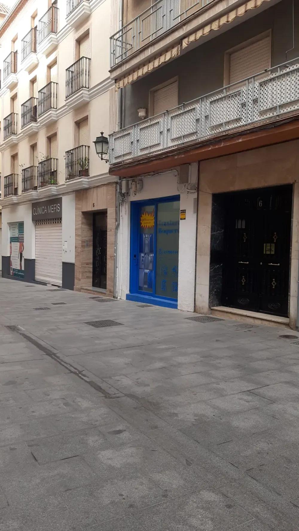 Vista a nivel de calle de una estrecha calle de la ciudad, flanqueada por edificios de varias plantas, con escaparates de marcos azules.