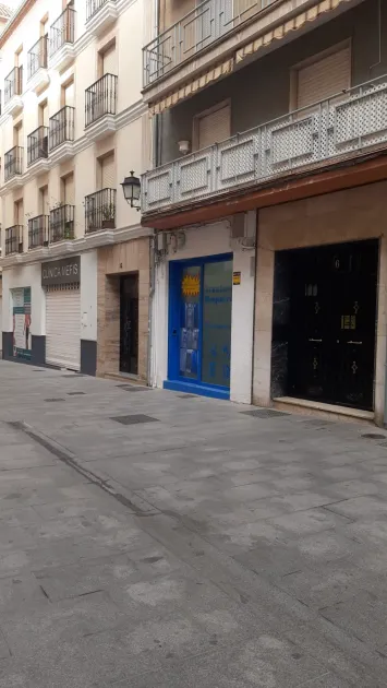 Vista a nivel de calle de una estrecha calle de la ciudad, flanqueada por edificios de varias plantas, con escaparates de marcos azules.