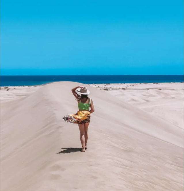 Una mujer camina sobre una duna de arena cerca del océano.