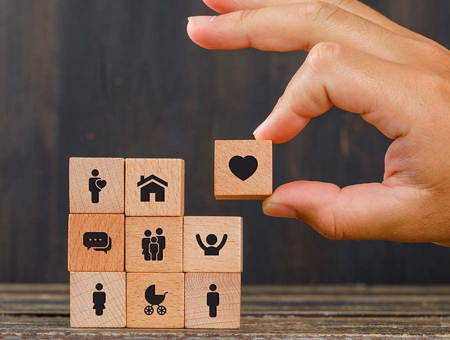 Una mano coloca un bloque en forma de corazón sobre bloques de madera apilados con iconos de hogar, familia y chat.