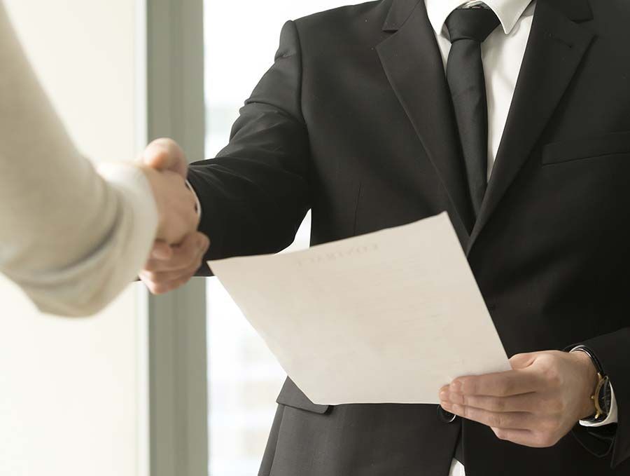 Empresario con traje negro estrechando la mano mientras sostiene un documento durante una reunión.