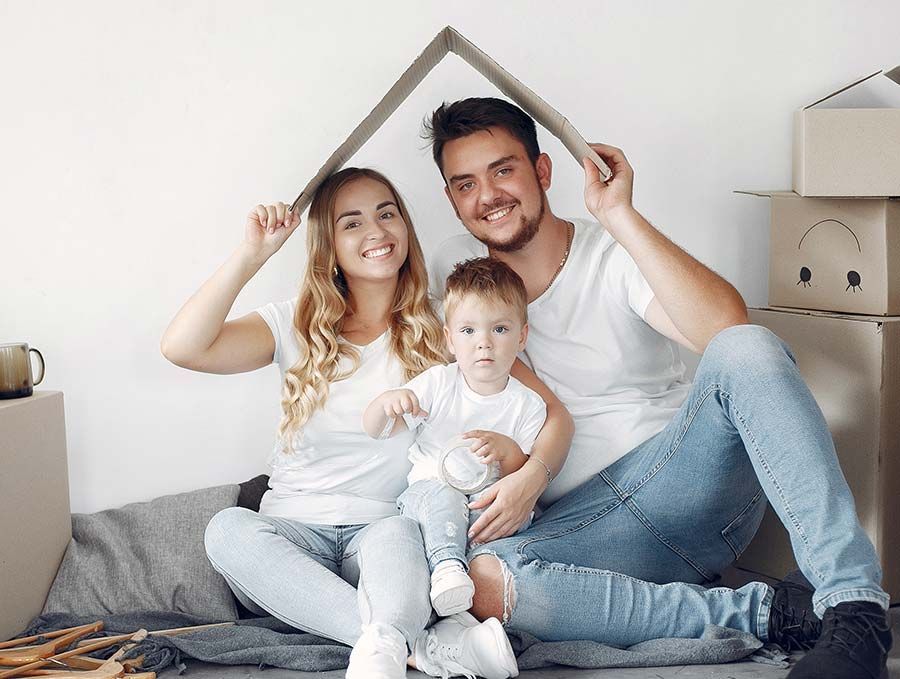 Una familia sonriente sentada en una cama, sosteniendo sobre ellos una estructura con forma de techo en una habitación luminosa.