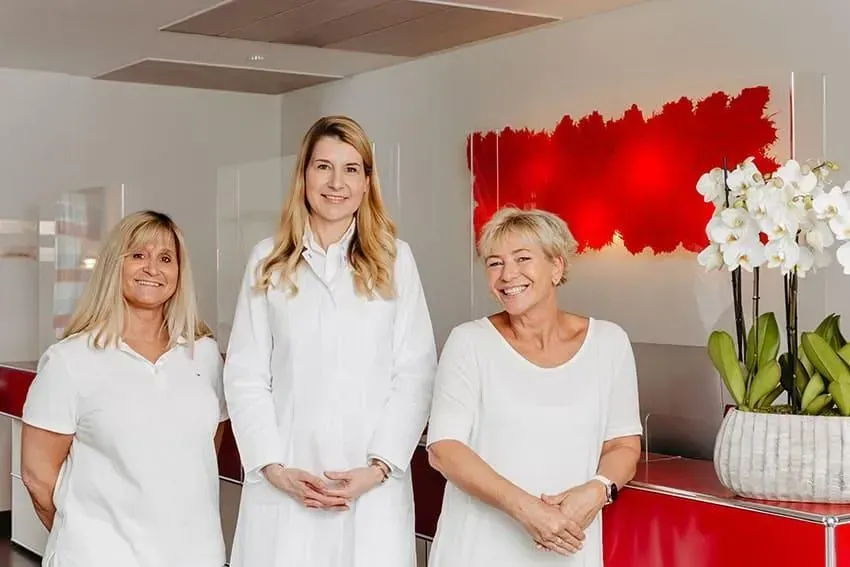Drei Frauen in weißen Outfits stehen nebeneinander in einem Raum. Dermatologie & Ästhetik | Dr. med. Kerstin Schatton