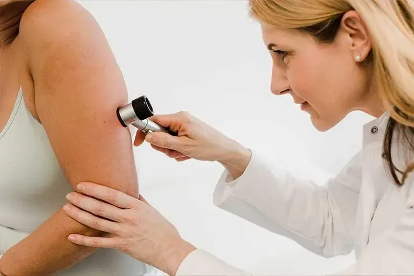 Ein Arzt untersucht den Arm einer Frau mit einer Lupe. Dermatologie & Ästhetik | Dr. med. Kerstin Schatton