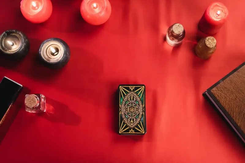 Mesa roja con velas encendidas, cartas de tarot y un libro.