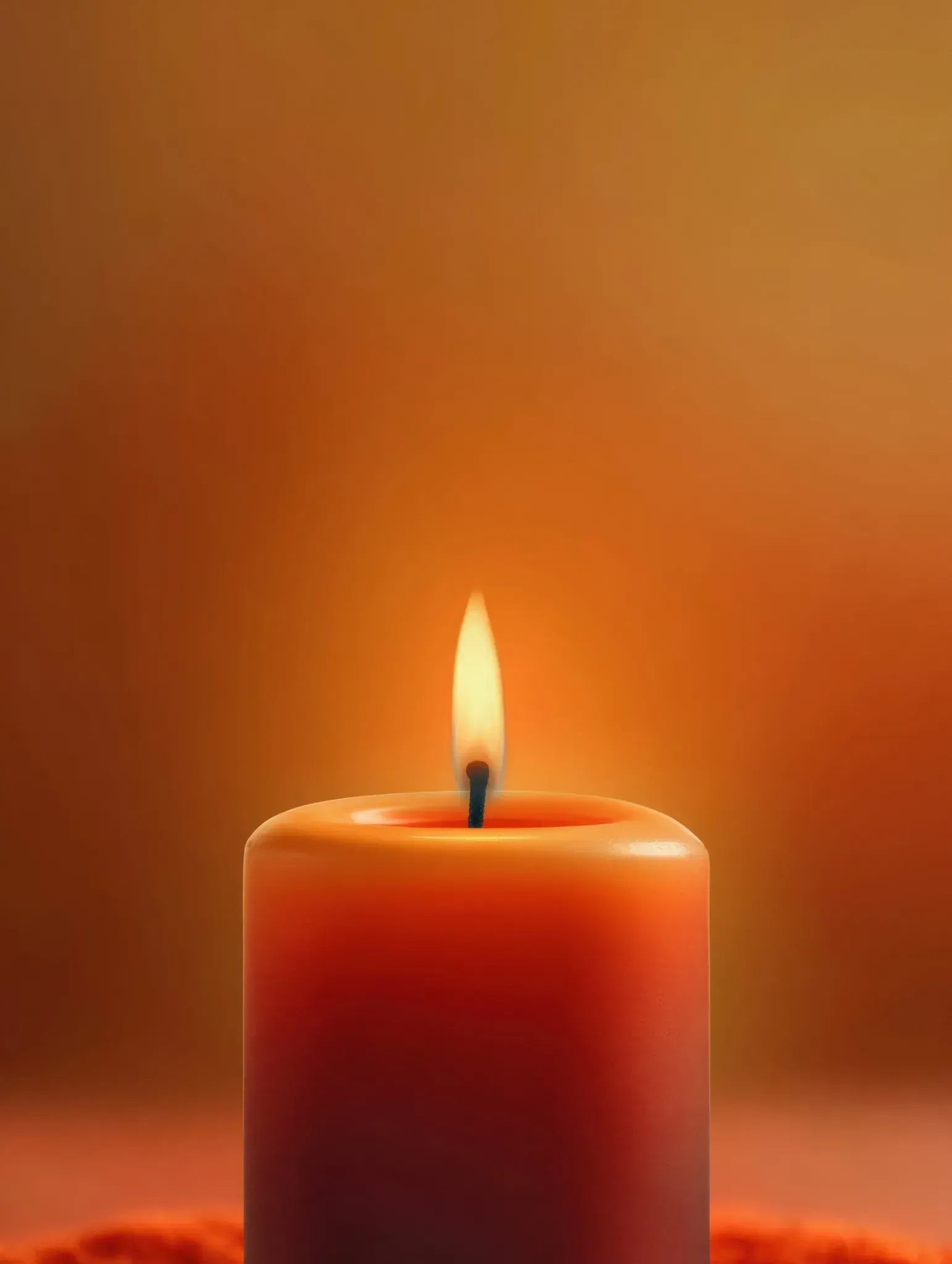 Vela naranja con llama encendida, brillo cálido sobre un fondo naranja borroso.