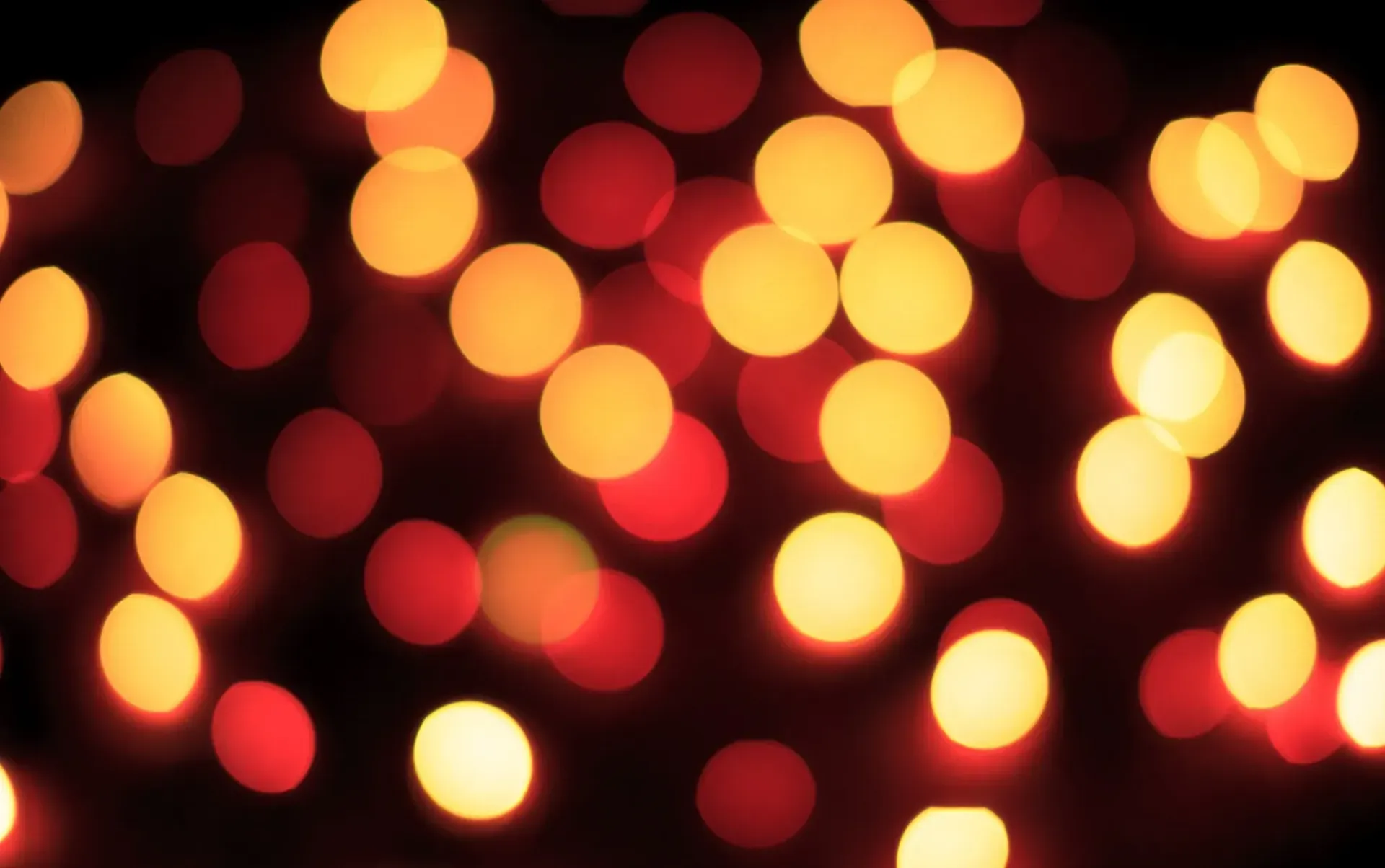 Luces cálidas y desenfocadas en tonos rojos y dorados sobre un fondo oscuro, que recuerdan a las luces navideñas.
