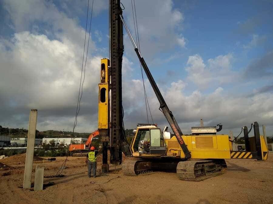 Un hombre está de pie junto a una gran excavadora amarilla en un sitio de construcción.