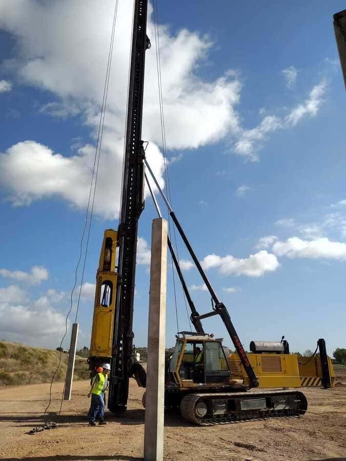 Un sitio de construcción con una grúa amarilla y un hombre parado junto a ella.