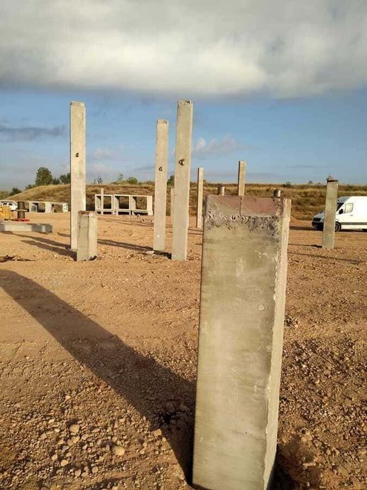 Una hilera de postes de hormigón se encuentran en un campo de tierra.