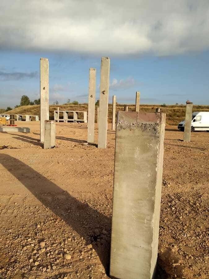 Una hilera de pilares de hormigón se encuentran sobre un campo de tierra.