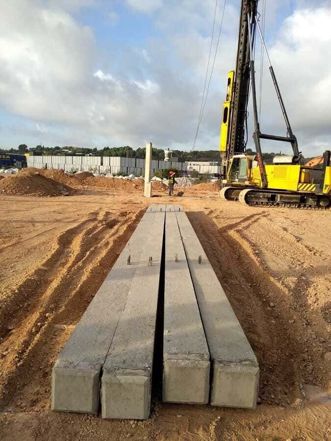 Una excavadora amarilla está levantando pilares de hormigón en un campo de tierra.