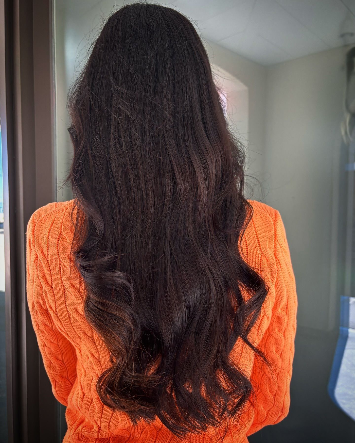 Eine Frau mit langen schwarzen Haaren trägt einen orangefarbenen Pullover.