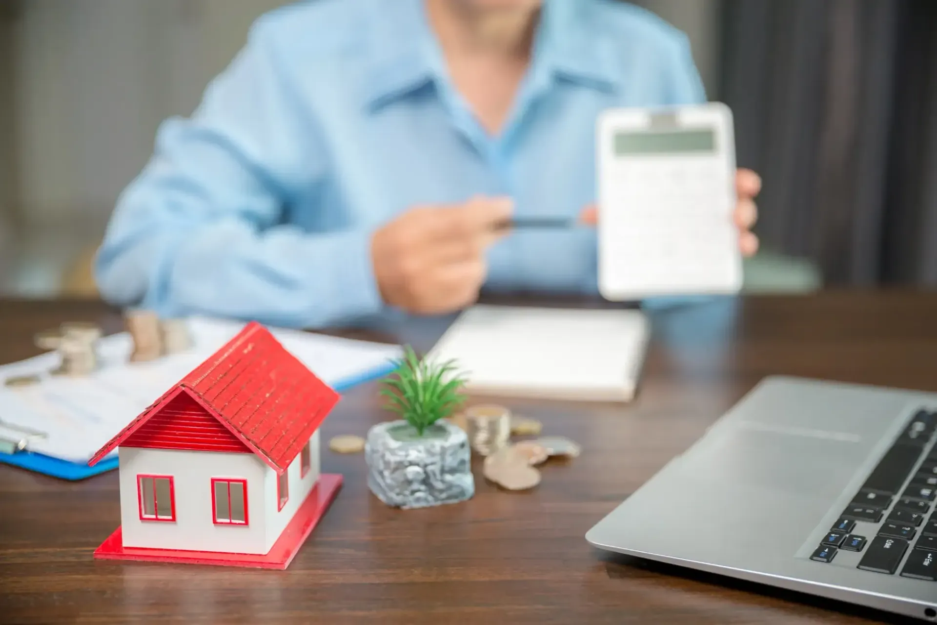 Casa en miniatura con techo rojo sobre un escritorio, calculadora, computadora