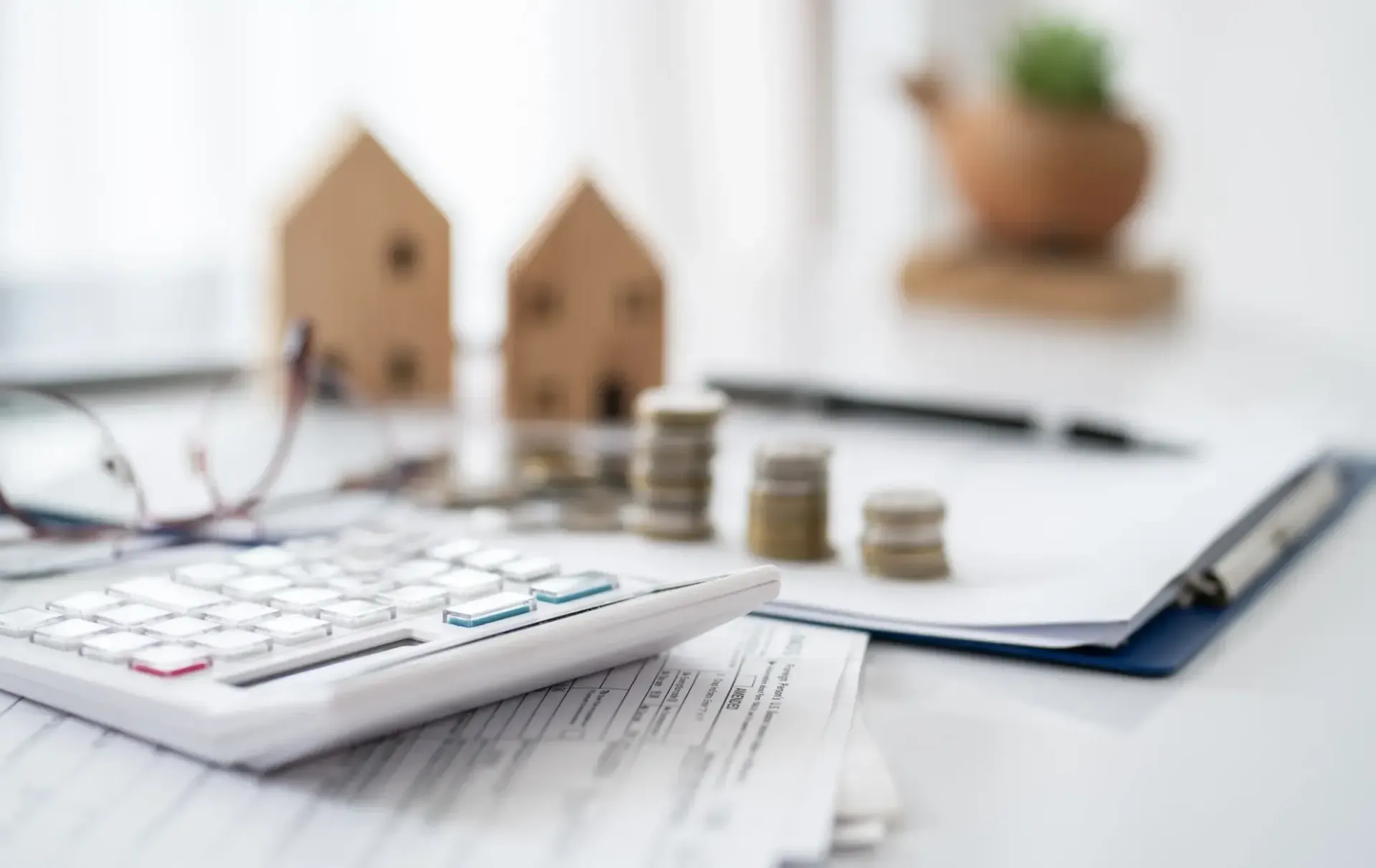 Calculadora, monedas, documentos y modelos de casas sobre una mesa blanca; concepto de planificación financiera.