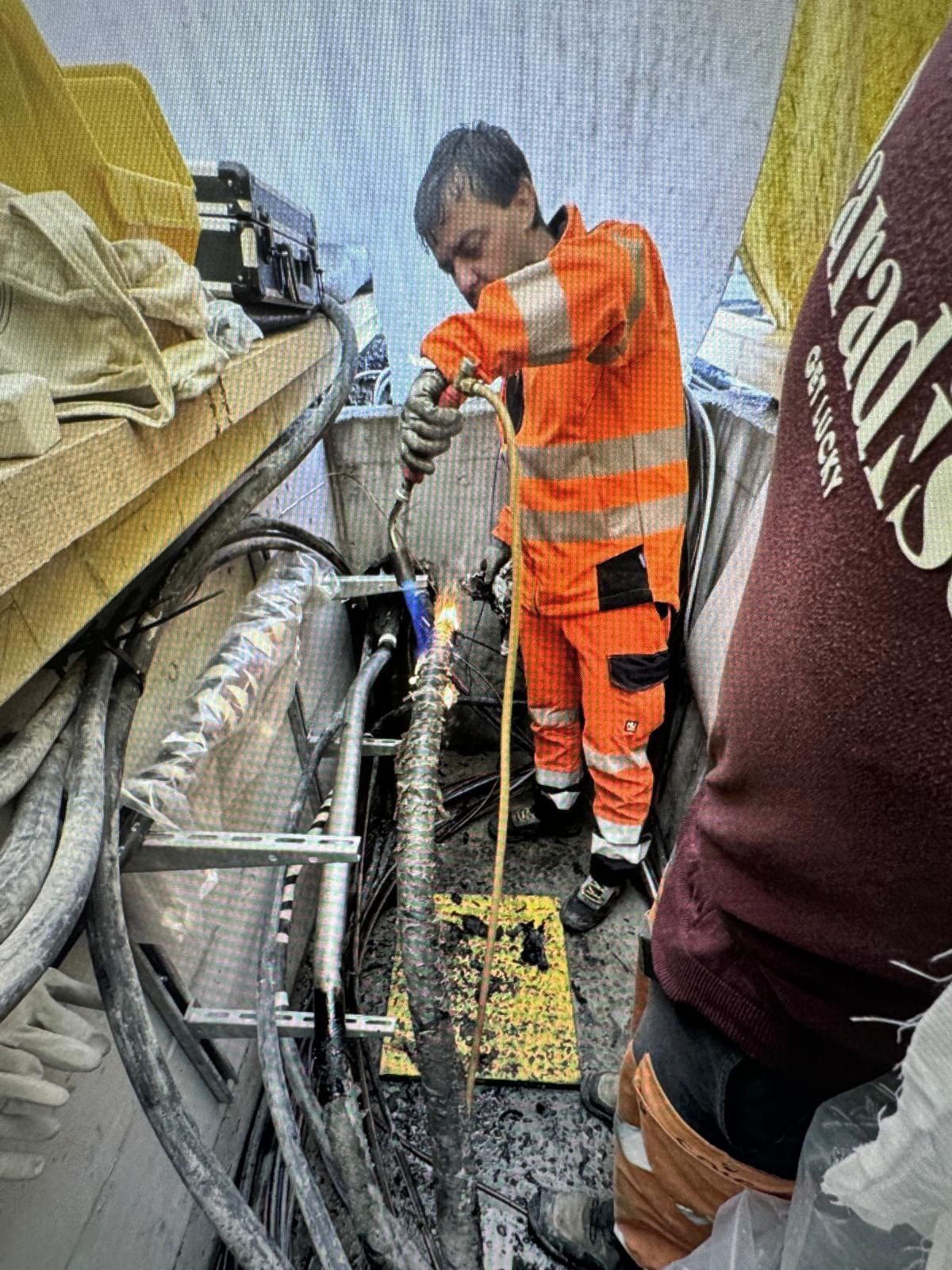 Un homme en combinaison de sécurité orange nettoie un tuyau avec une serpillère.