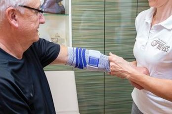 Mitarbeiterin der Orthopädie-Schuhtechnik Huber hilft einem Patienten mit einer Bandage