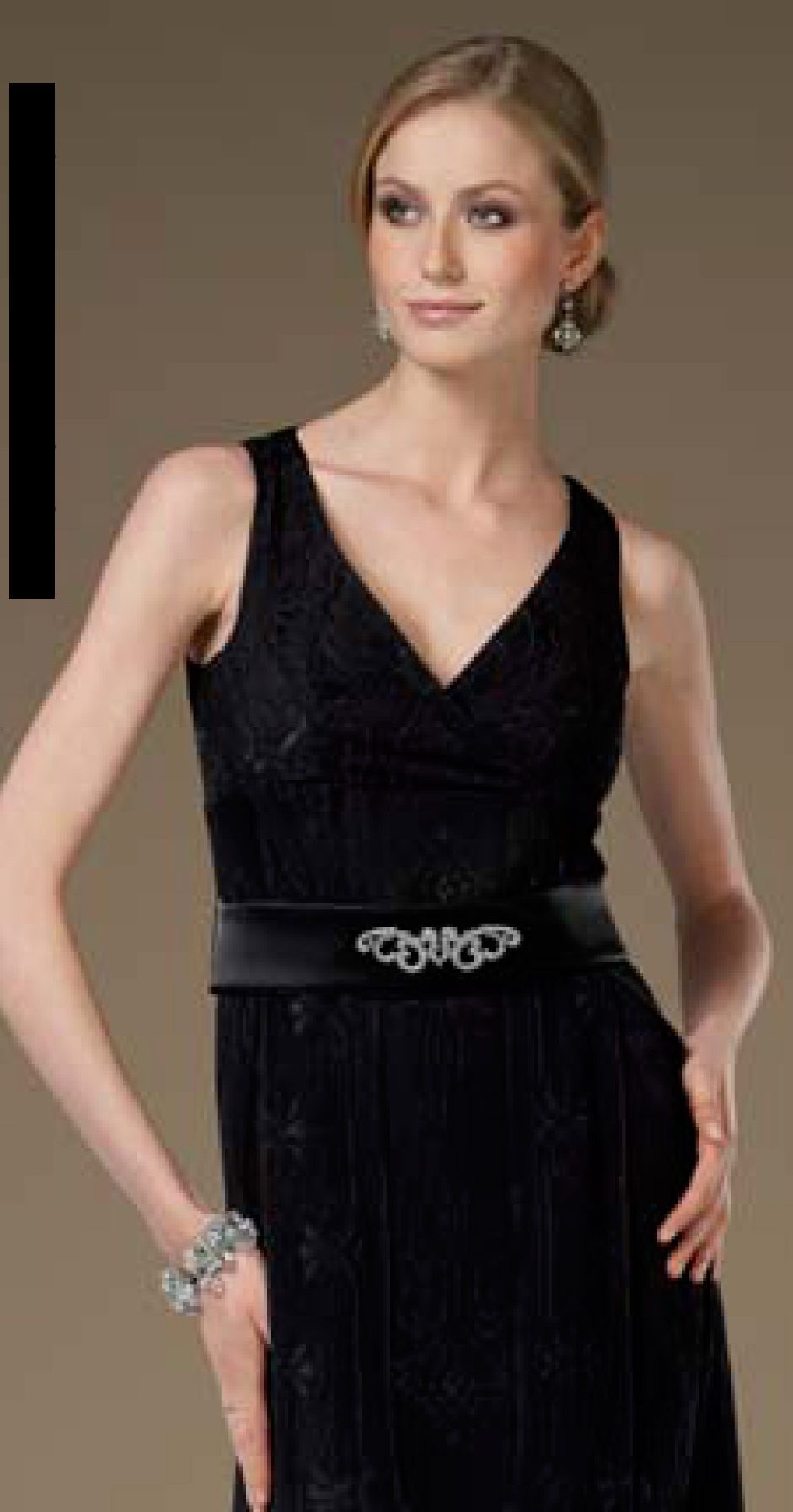 Frau in einem schwarzen Kleid mit V-Ausschnitt und verziertem Gürtel, stehend in einem Innenraum.