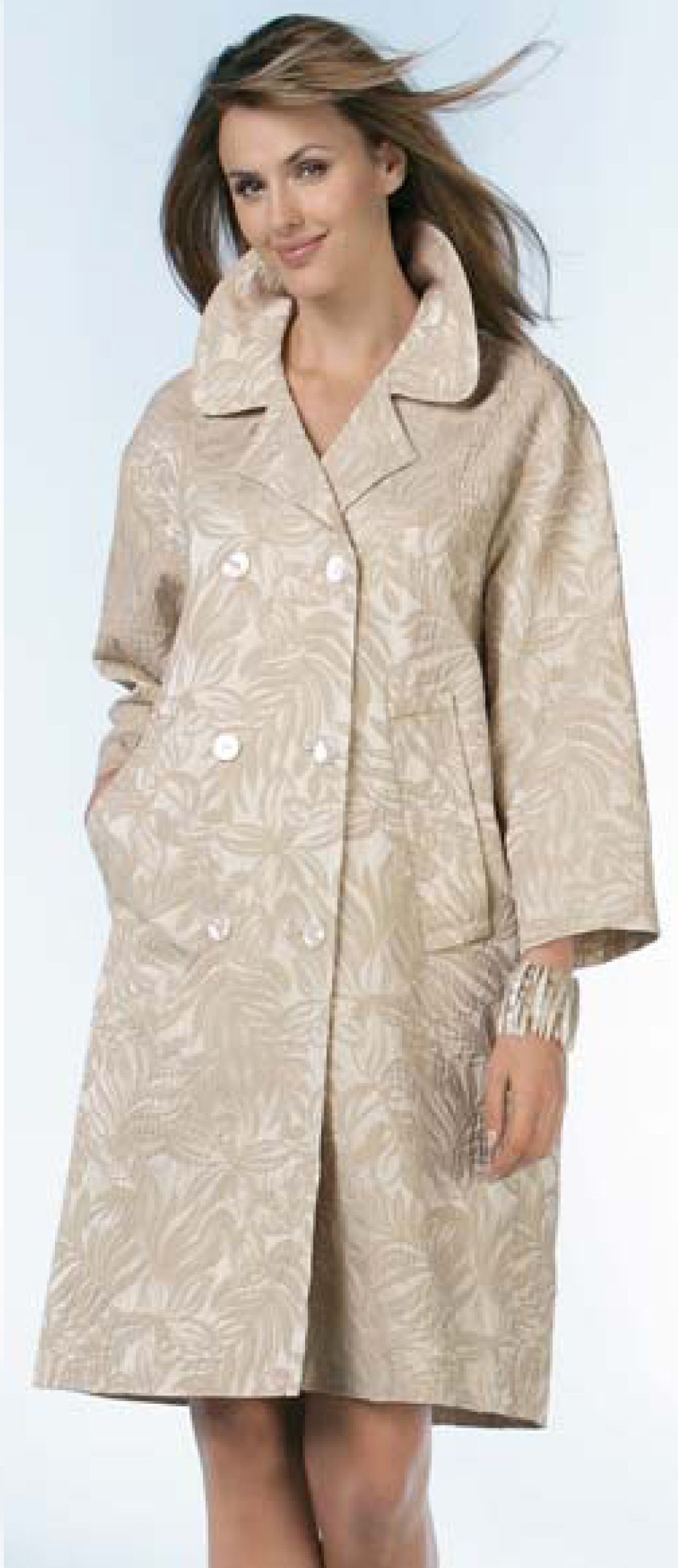 Frau in einem knielangen, hellbraunen, gemusterten Mantel. Sie lächelt vor hellblauem Hintergrund.