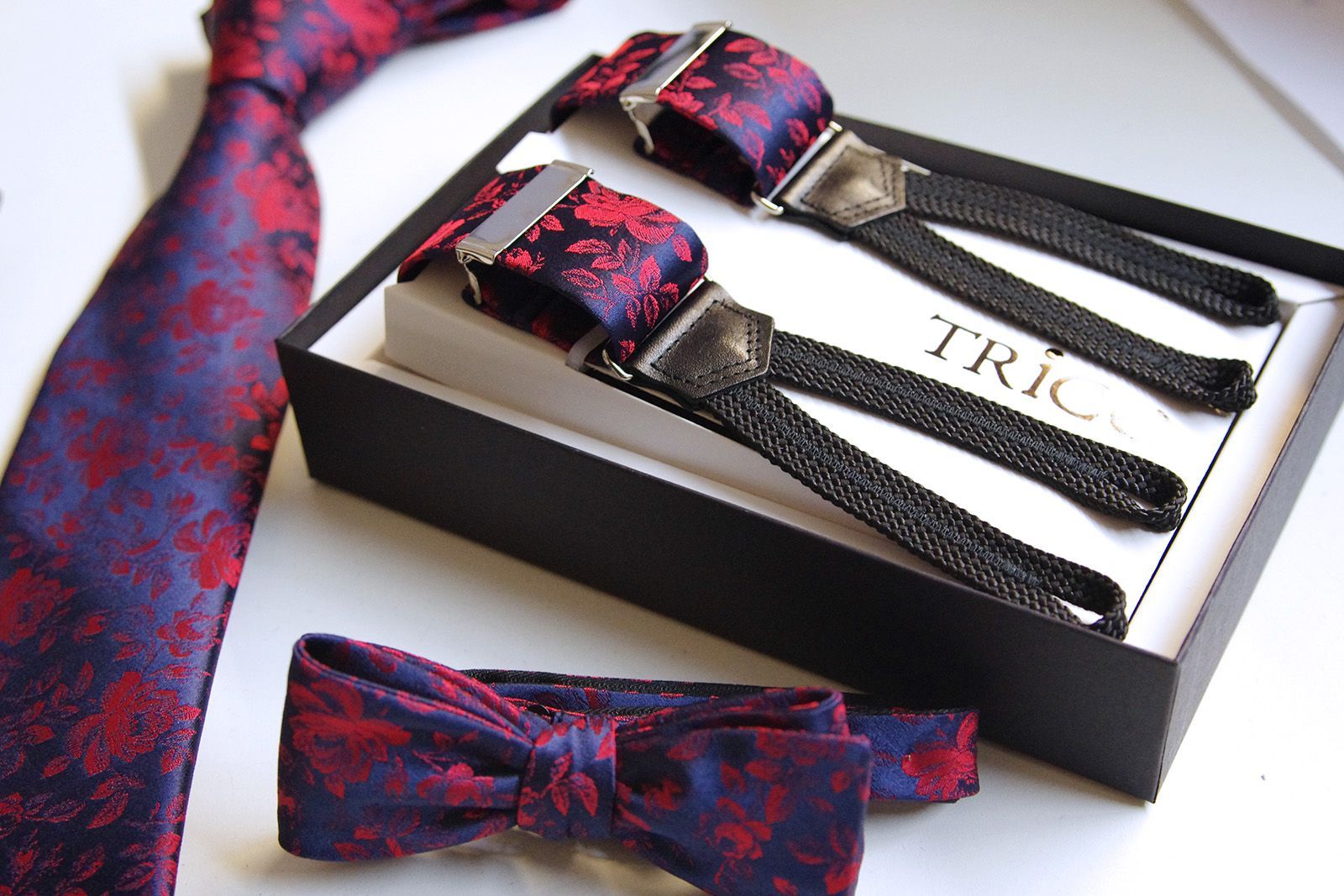 Herrenaccessoires-Set: Krawatte, Hosenträger und Fliege, mit rotem Blumenmuster auf blauem Grund, in einer schwarzen Schachtel.