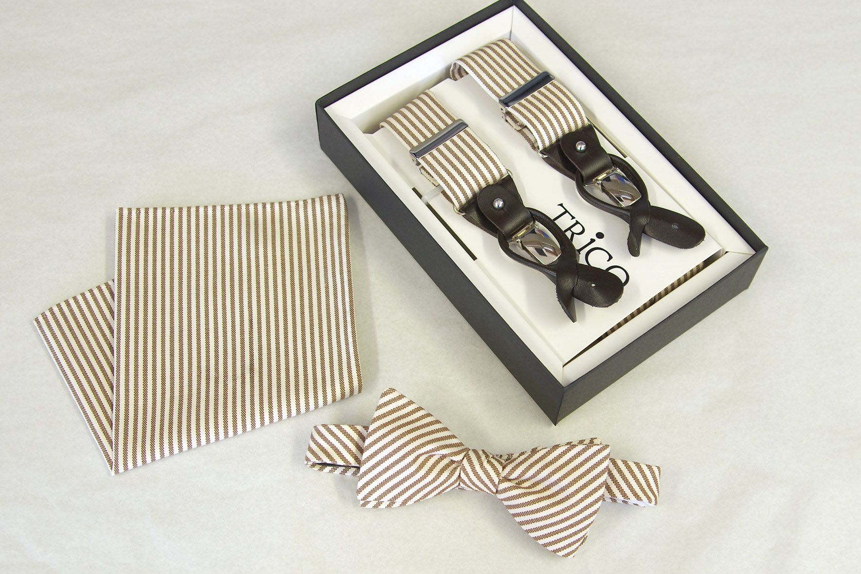 Hellbraun gestreifte Hosenträger, Fliege und Einstecktuch in einer Schachtel.