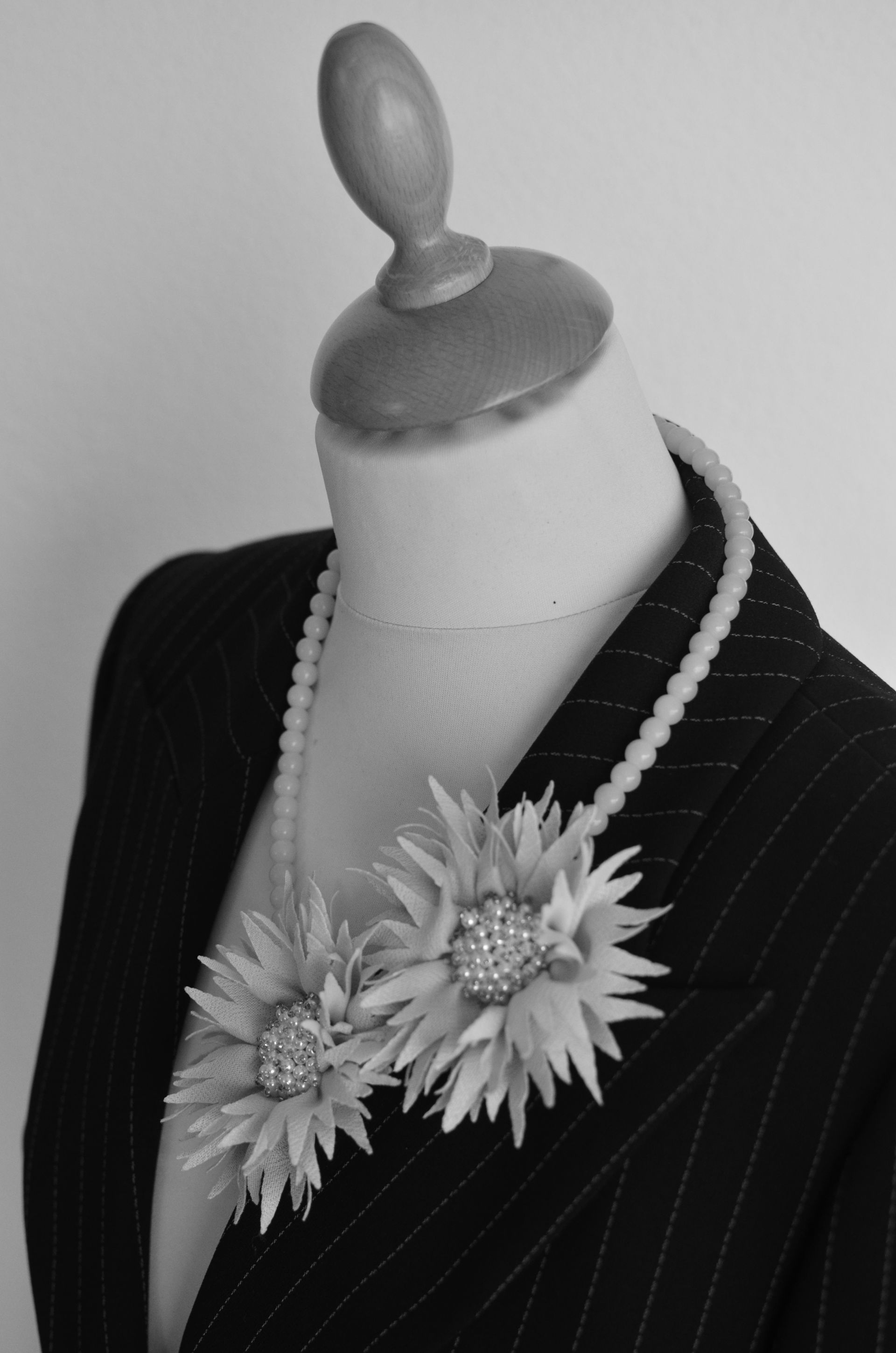 Schaufensterpuppe in einem Nadelstreifenblazer, die eine Perlenkette mit zwei Blumenbroschen trägt.