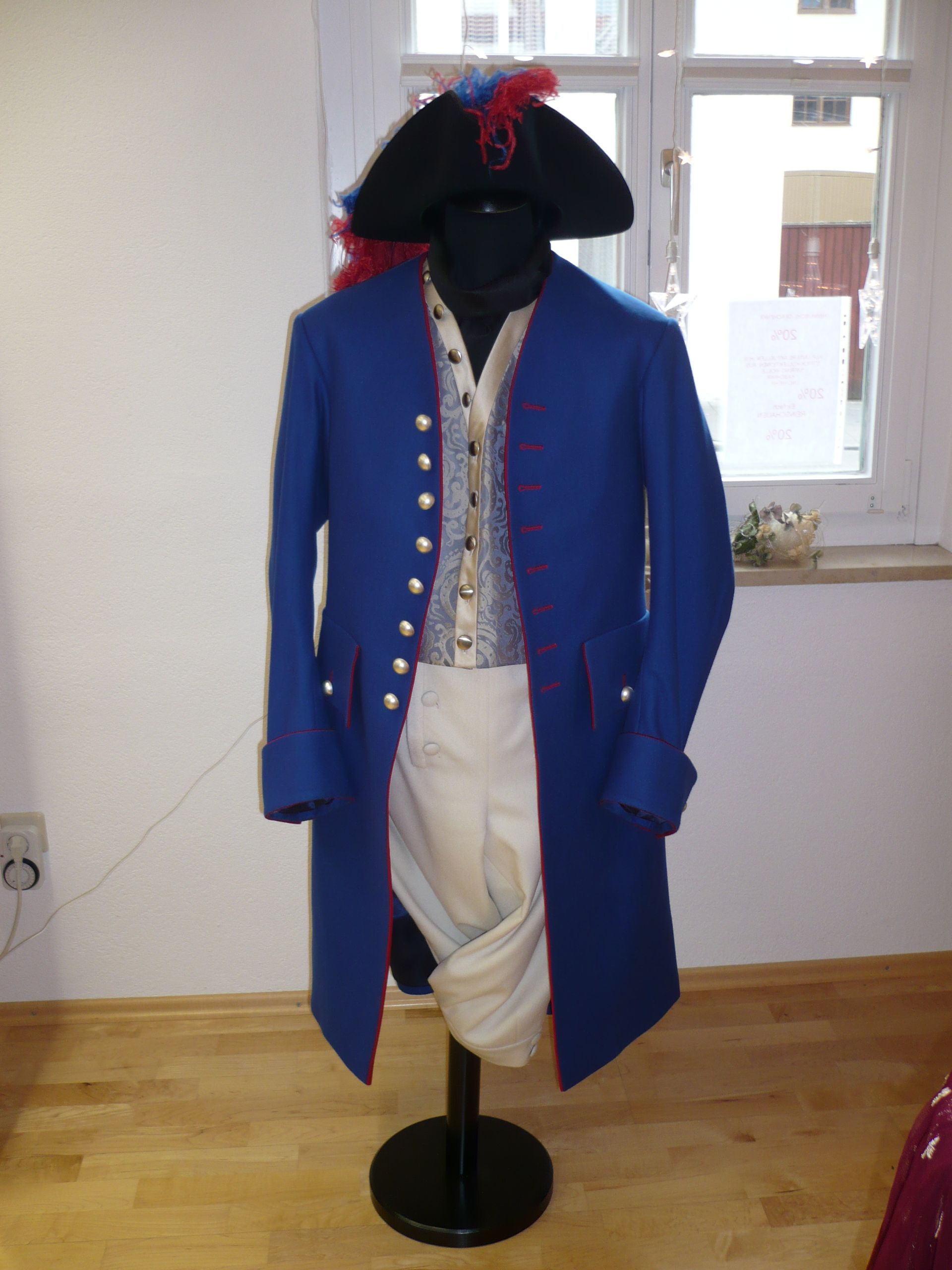 Eine Schaufensterpuppe trägt einen braun-goldenen Mantel mit einer weißen Spitzenkrawatte.