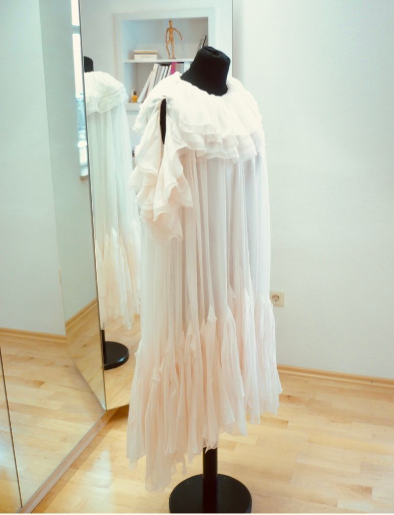 Weißes, fließendes Kleid an einer schwarzen Schaufensterpuppe vor einer hellen Wand mit teilweiser Spiegelung.