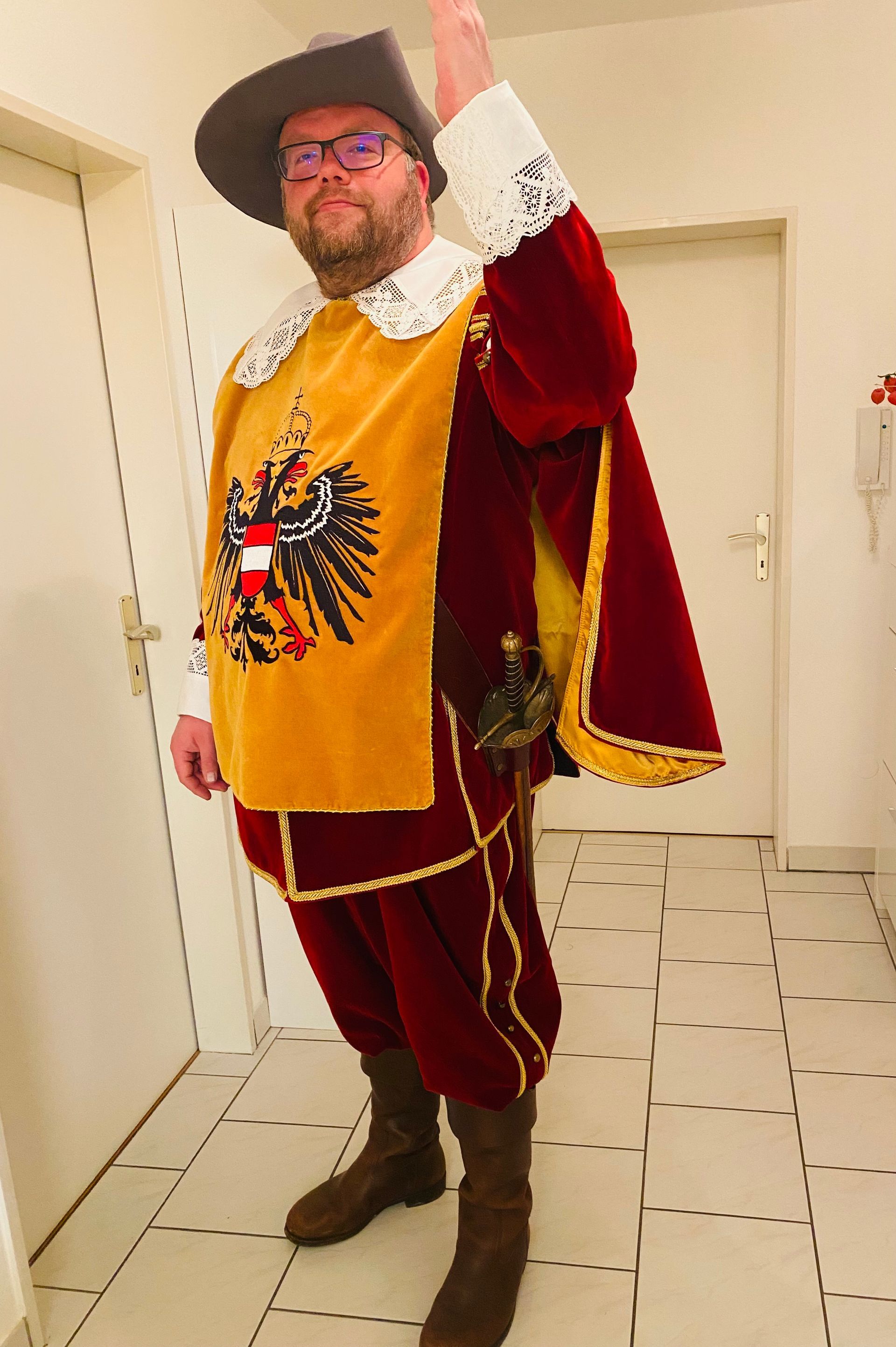 Mann in historischer österreichischer Tracht hebt die Hand. Gelb-rotes Ensemble, Hut.