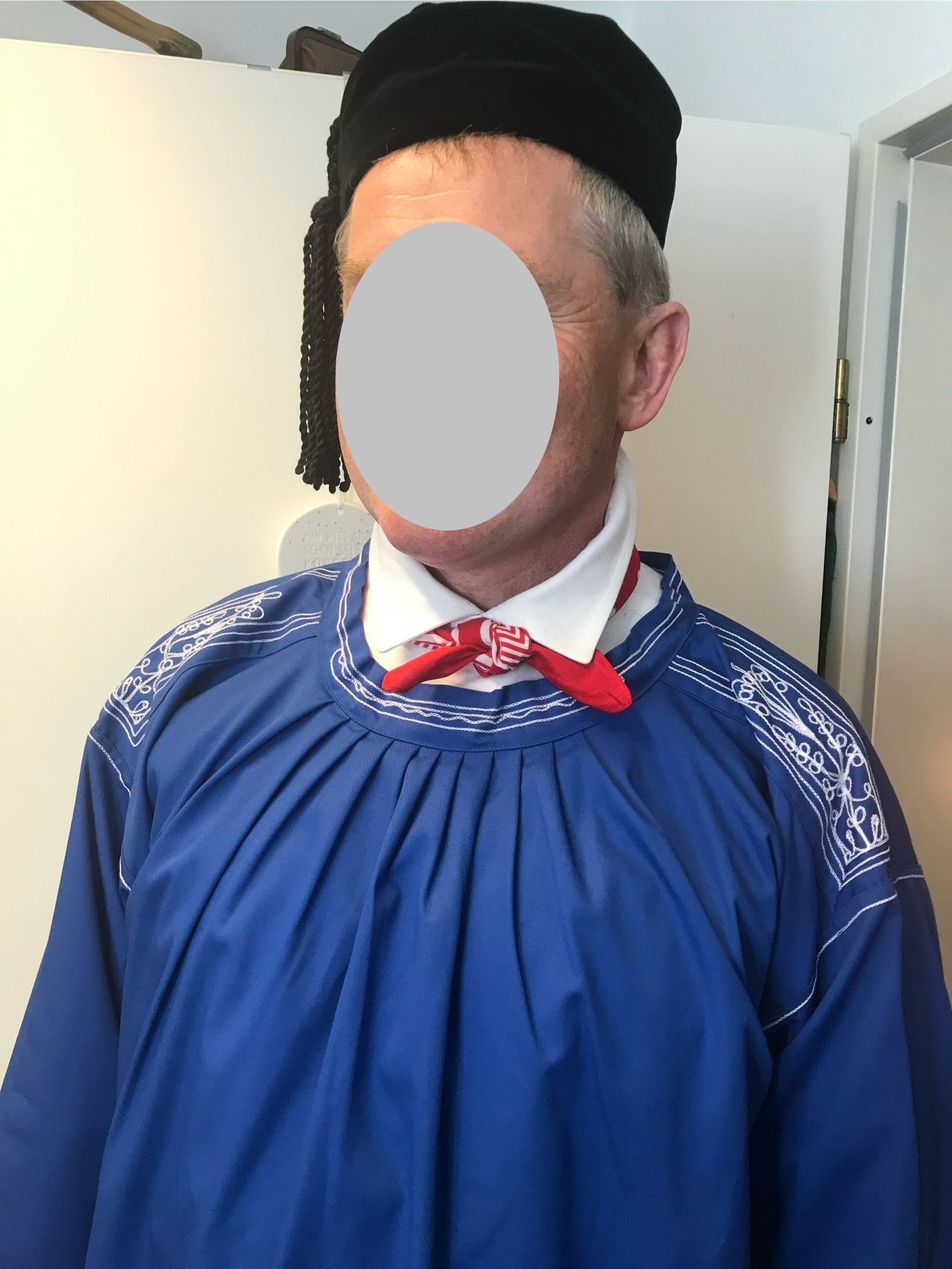 Person in blauem Hemd, weißem Kragen, roter Krawatte und schwarzem Hut.