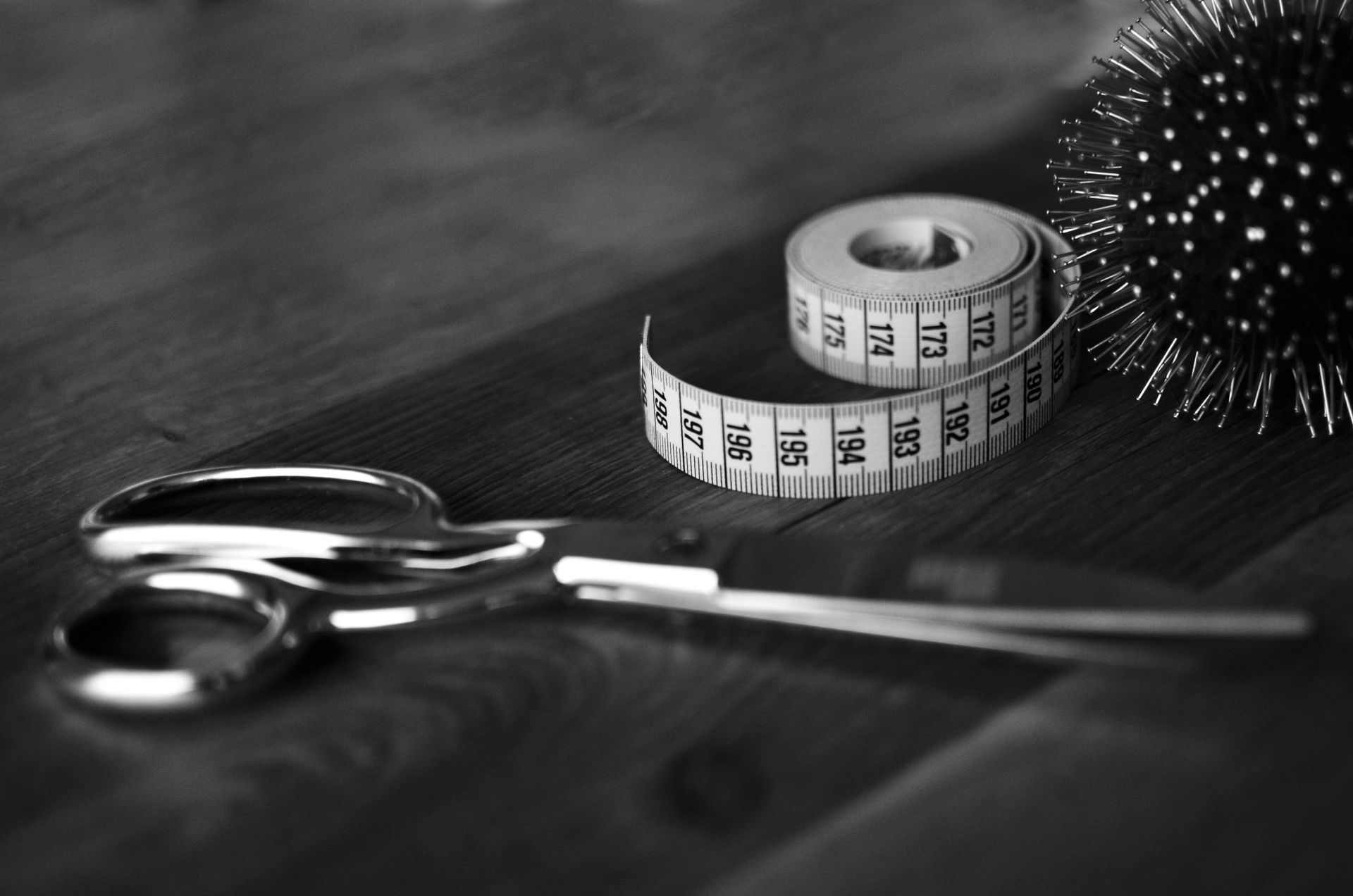 Schere, Maßband und Nadelkissen auf einer Holzoberfläche.