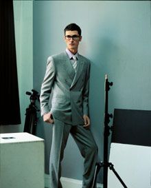 Ein Mann im Anzug und mit Sonnenbrille steht mit den Händen in den Taschen da.