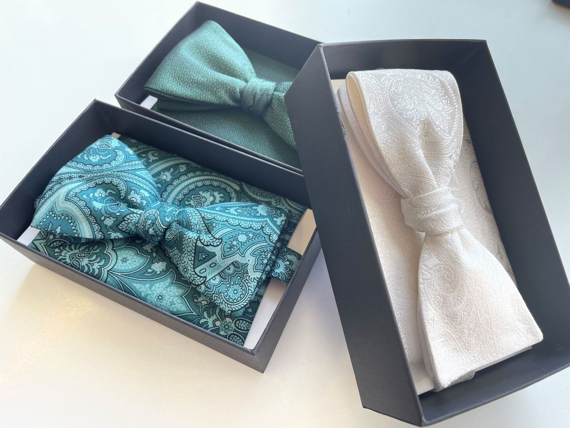 Drei Fliegensets in schwarzen Schachteln: türkis mit Paisleymuster, grün mit Strukturmuster und glit