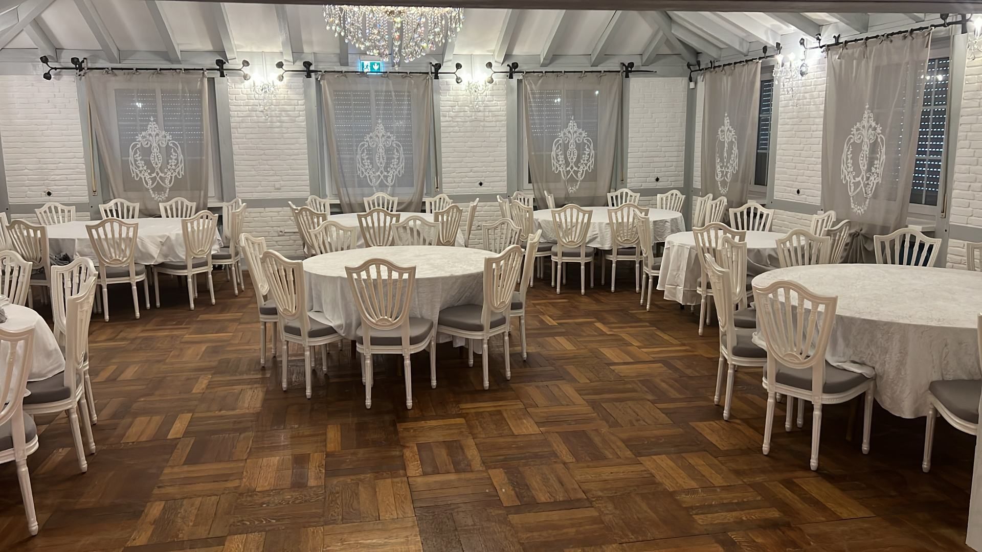 Eleganter Speisesaal mit runden Tischen für die Gäste; weiße Einrichtung, Holzboden.