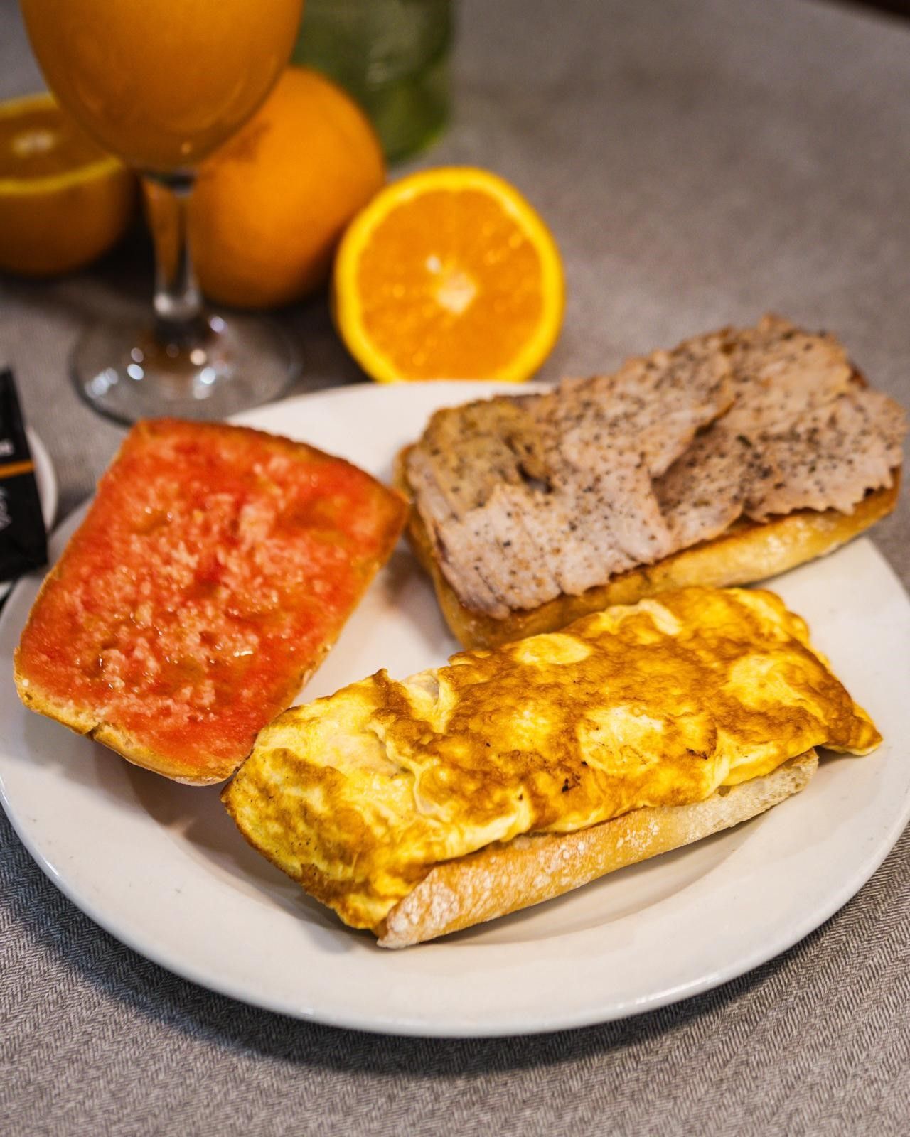 Un plato de desayuno con una tostada con tomate, una tostada con carne y una tostada con tortilla.