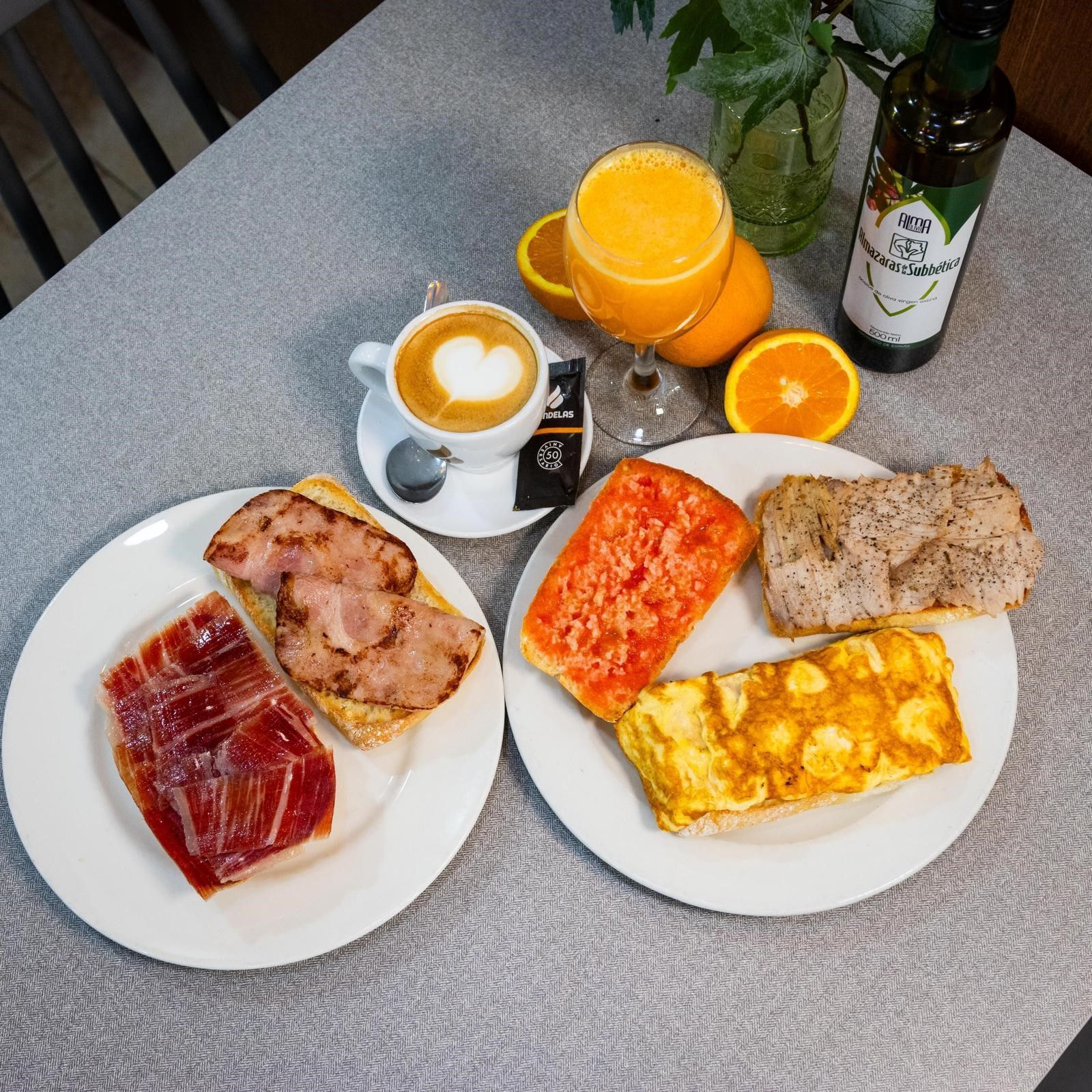 Un desayuno completo con café, zumo de naranja y dos platos de pan tostado con carne, huevo y tomate.