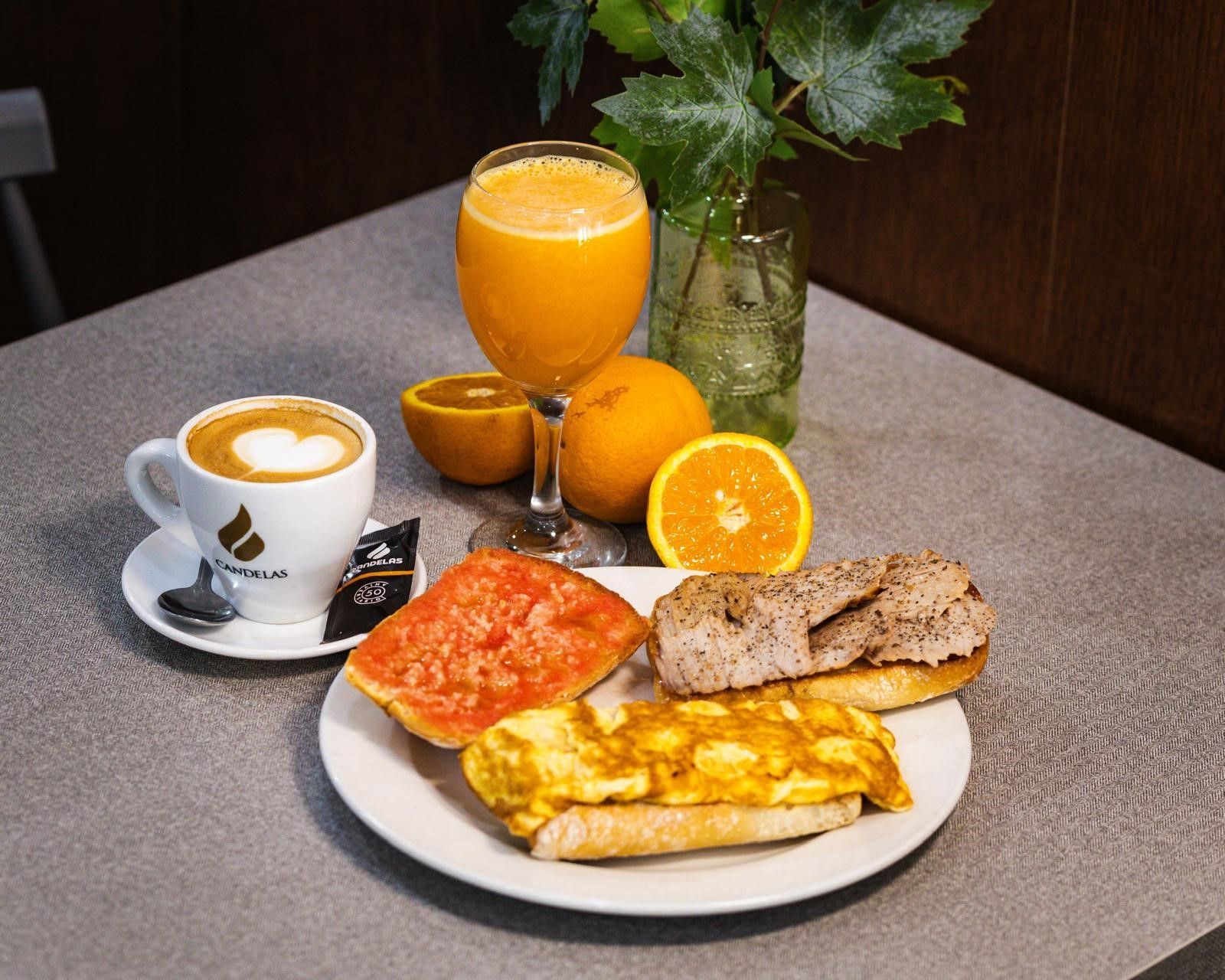Una rebanada de pan tostado con tomate, un vaso de zumo de naranja y una taza de café humeante sobre una mesa de madera.