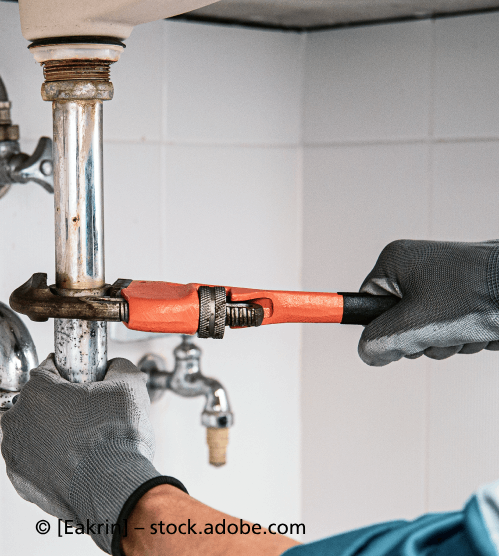 Ein Klempner repariert mit einem Schraubenschlüssel ein Rohr unter einem Waschbecken. R & I Felber Service GmbH