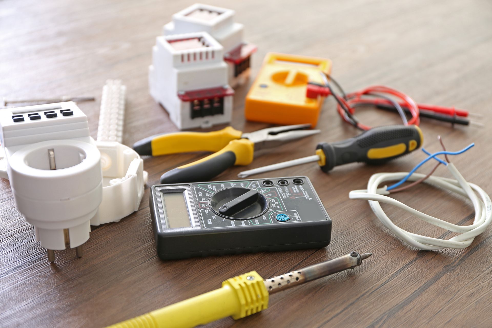 Outils électriques et fils sur une table en bois, notamment une pince, un multimètre et des connecteurs de câbles.