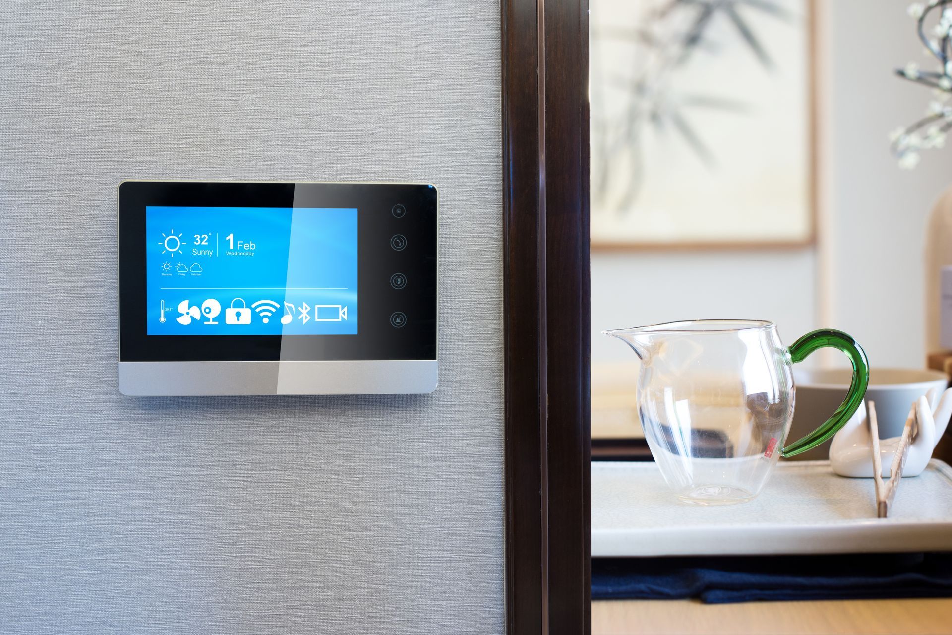 Thermostat mural à écran tactile à côté d'une table à manger avec un pichet et des tasses en verre dans une pièce lumineuse