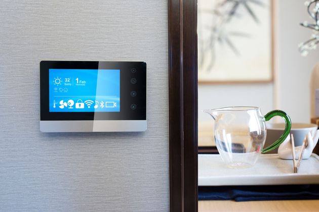 Thermostat mural à écran tactile à côté d'une table à manger avec un pichet et des tasses en verre dans une pièce lumineuse