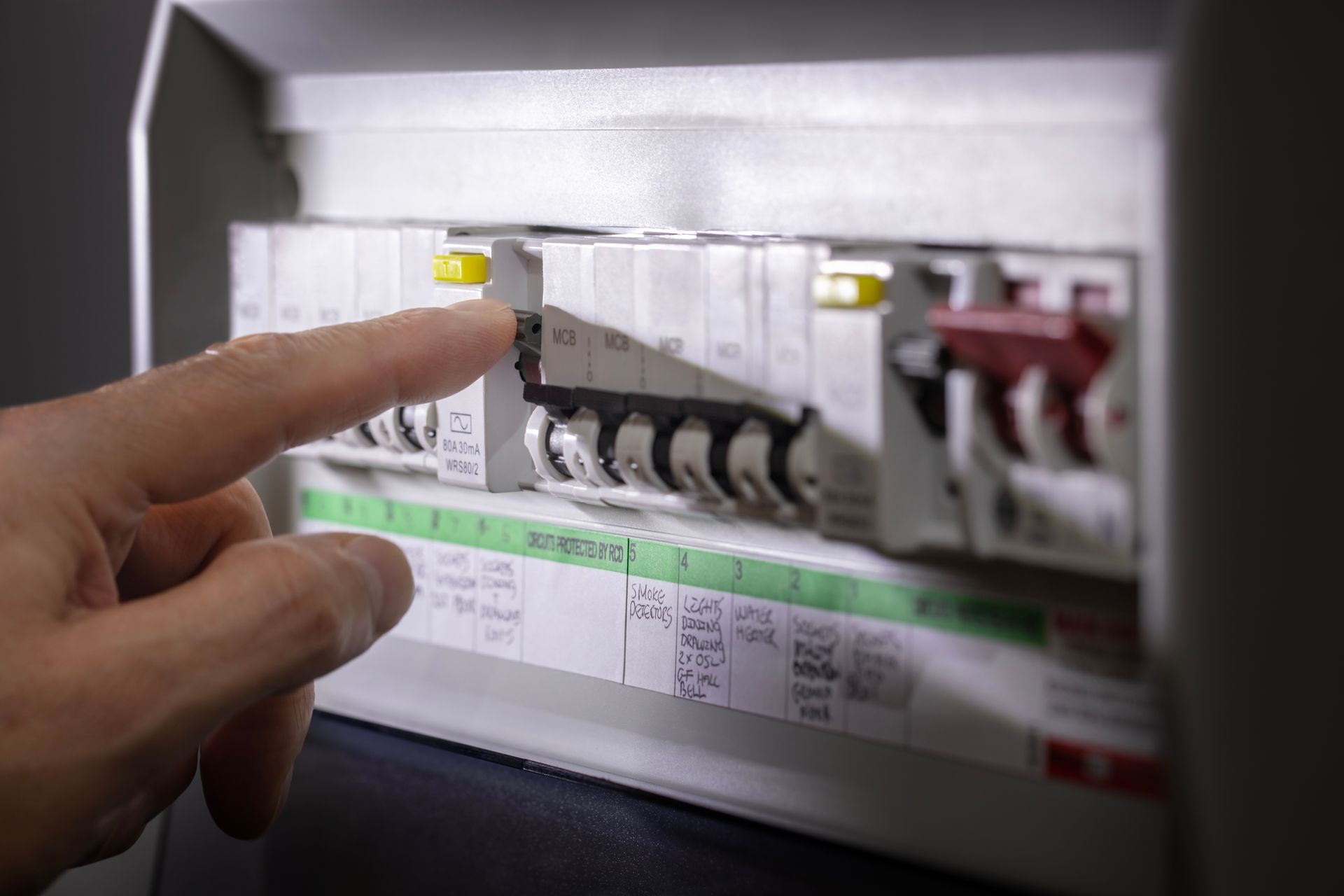 Une personne appuie sur un interrupteur dans un tableau de disjoncteurs électriques étiquetés