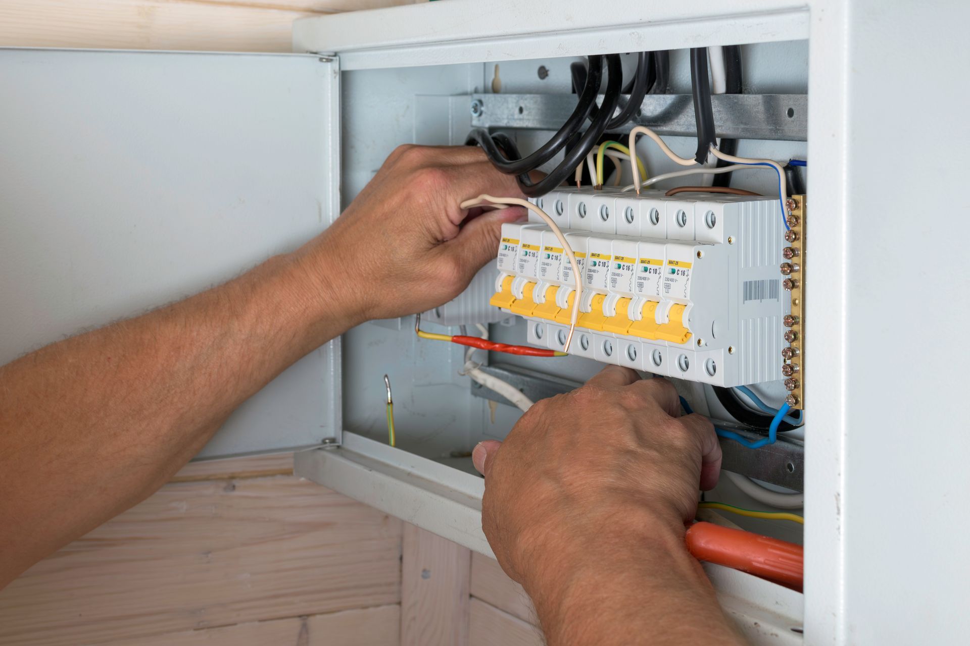 Un technicien effectue le câblage d'un tableau électrique à l'intérieur d'une armoire murale blanche.
