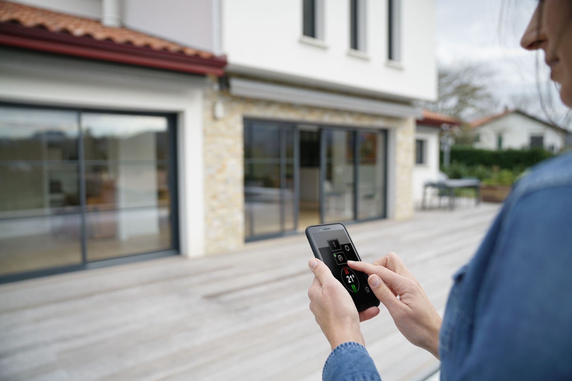 Une personne utilise un smartphone pour contrôler l'extérieur d'une maison moderne depuis sa terrasse.