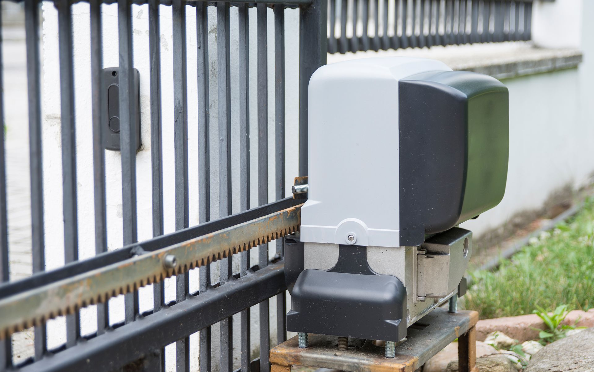 Moteur de portail coulissant automatique monté à côté d'une clôture métallique noire sur une base en béton.